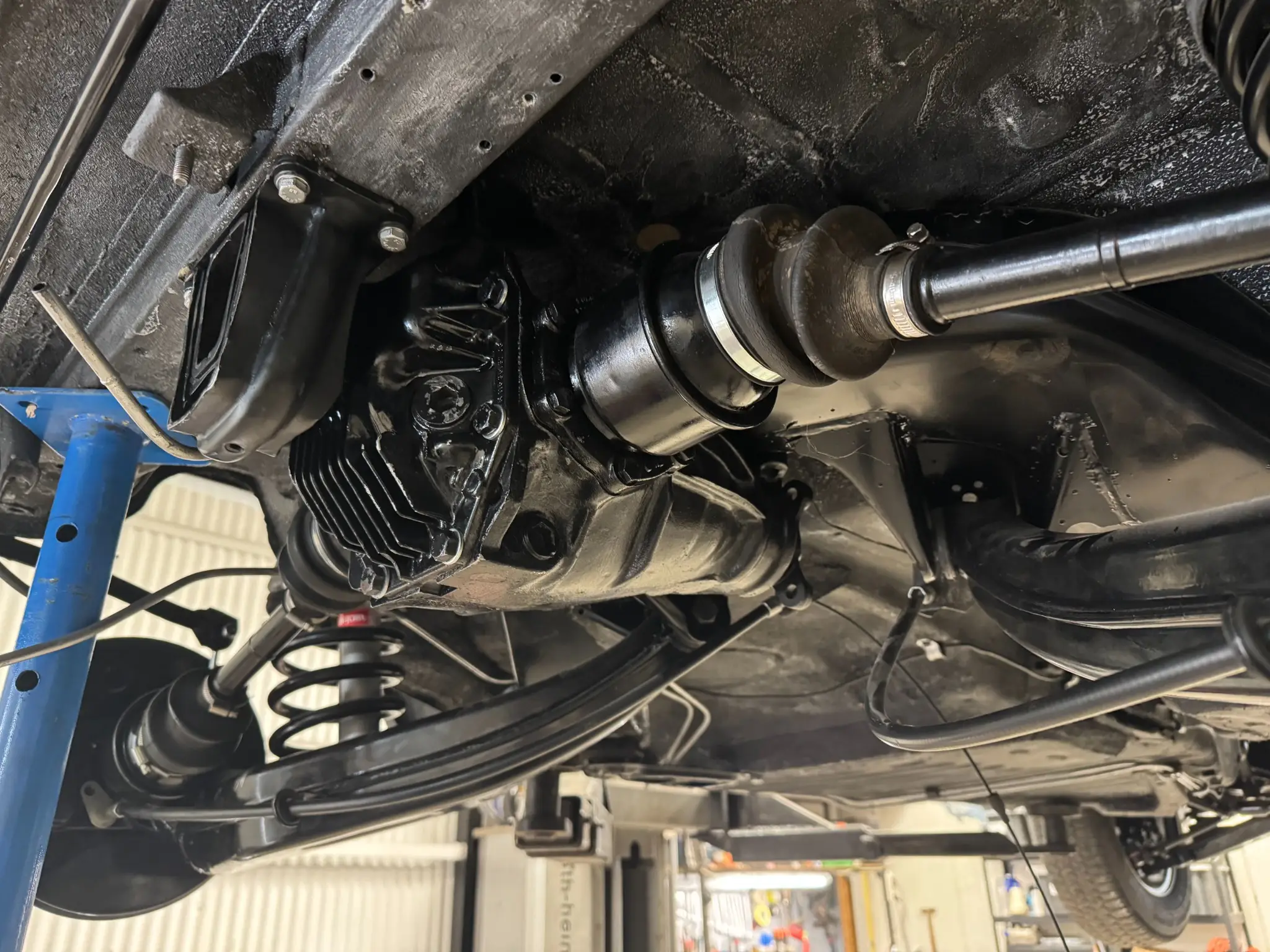 Widok od spodu na zawieszenie i układ napędowy samochodu na podnośniku warsztatowym, pokazujący dyferencjał, półosie i sprężyny tylnego zawieszenia.