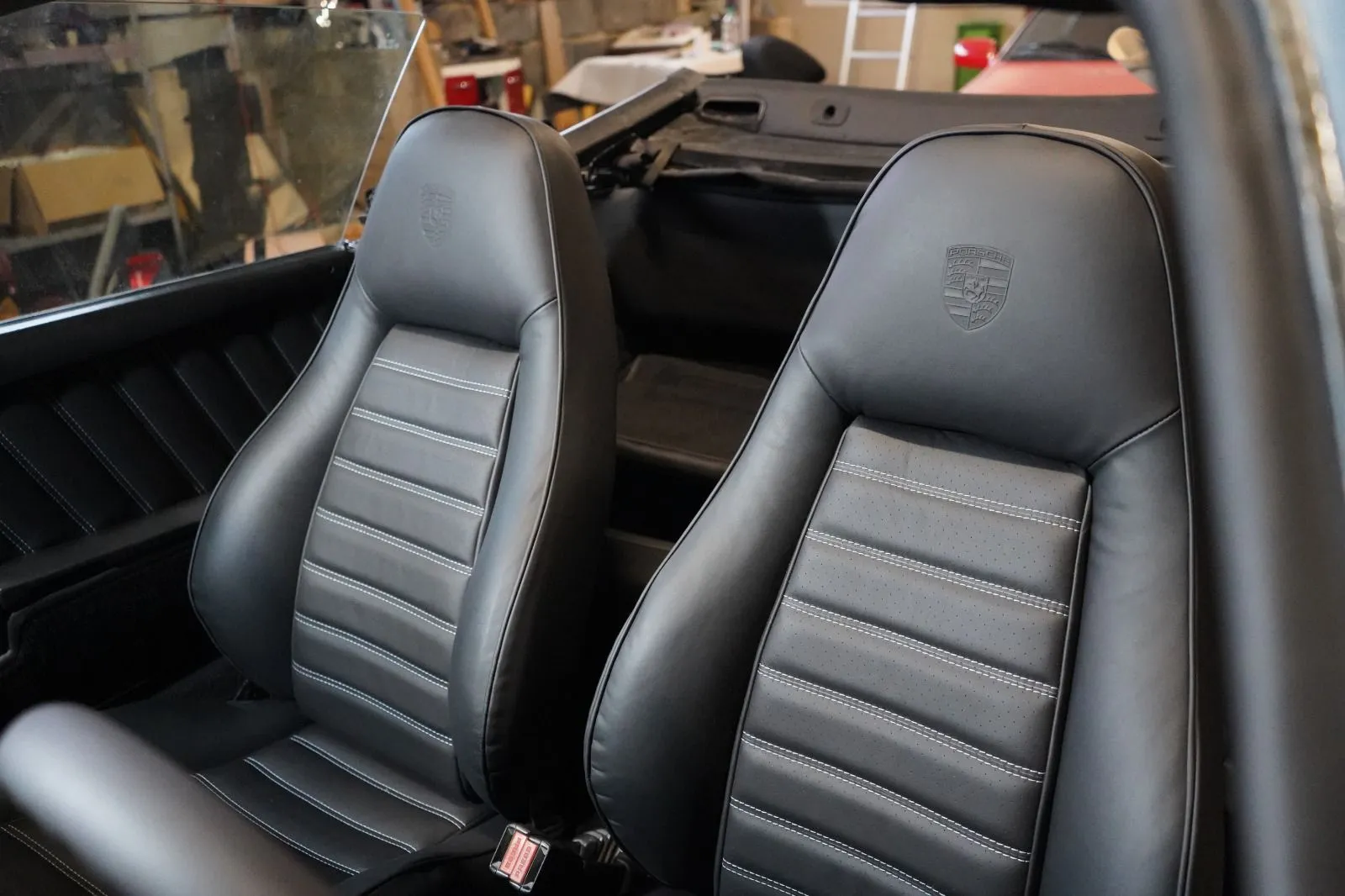 Wnętrze klasycznego samochodu sportowego z czarnymi skórzanymi fotelami z przeszyciami i wytłoczonym logo Porsche na zagłówkach.