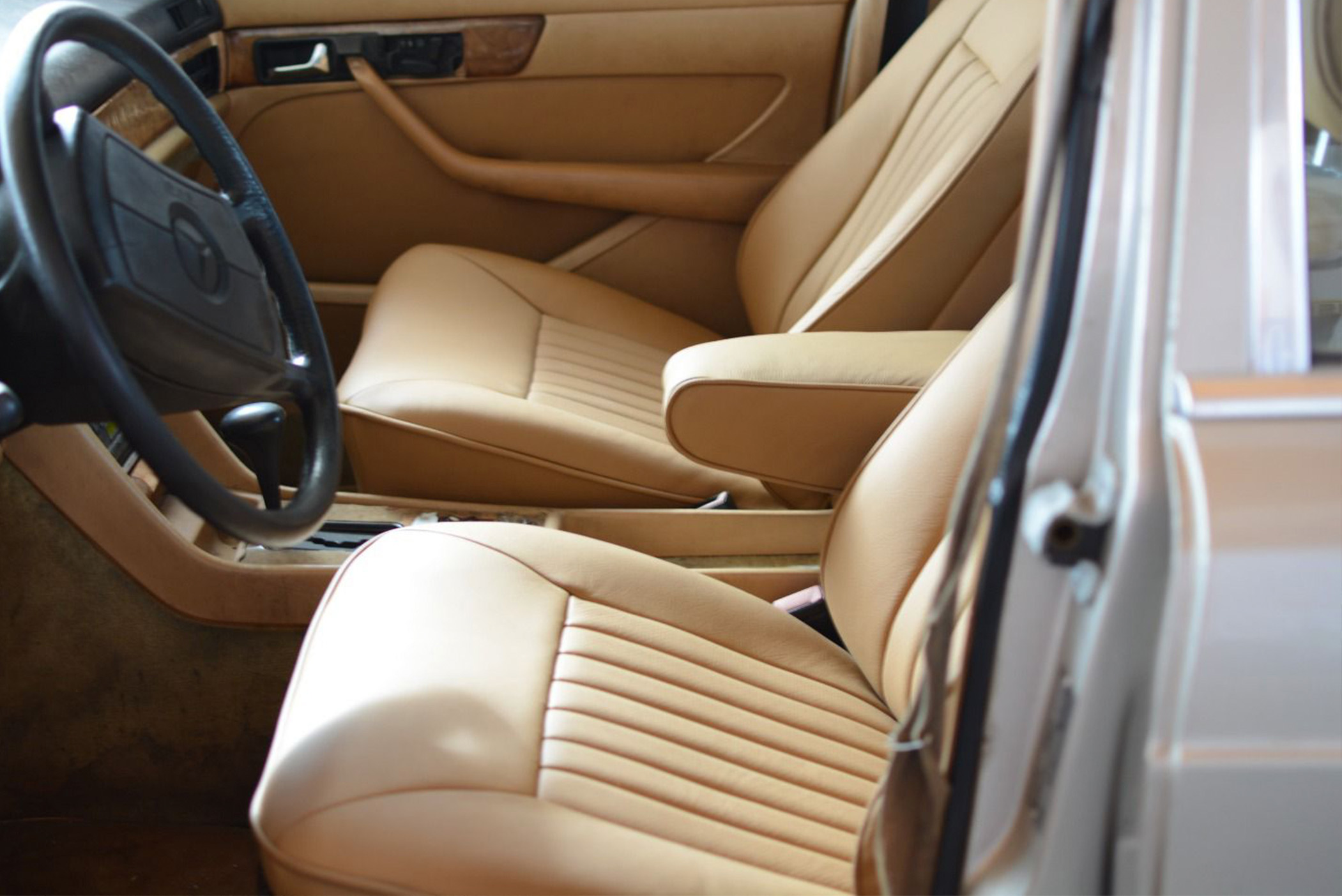 Wnętrze klasycznego samochodu z beżową, skórzaną tapicerką i czarną kierownicą.