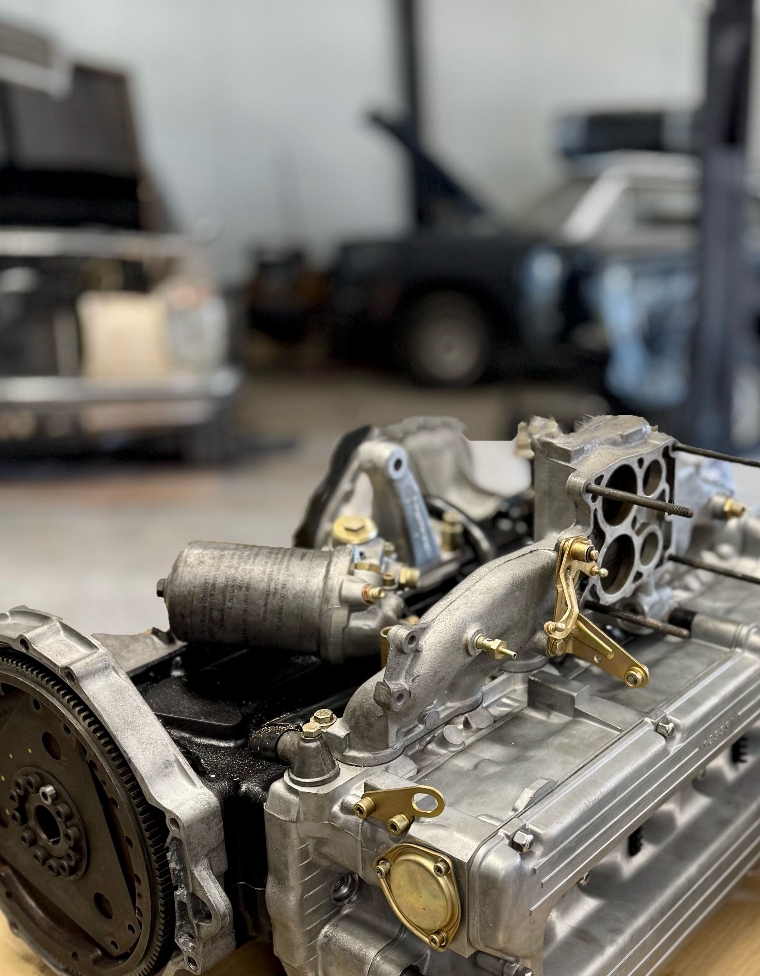 Zbliżenie na silnik samochodowy w warsztacie, z widocznymi metalowymi i mosiężnymi elementami.